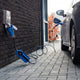 Coiled charging cable plugged into a wall socket beside a dark car on paving